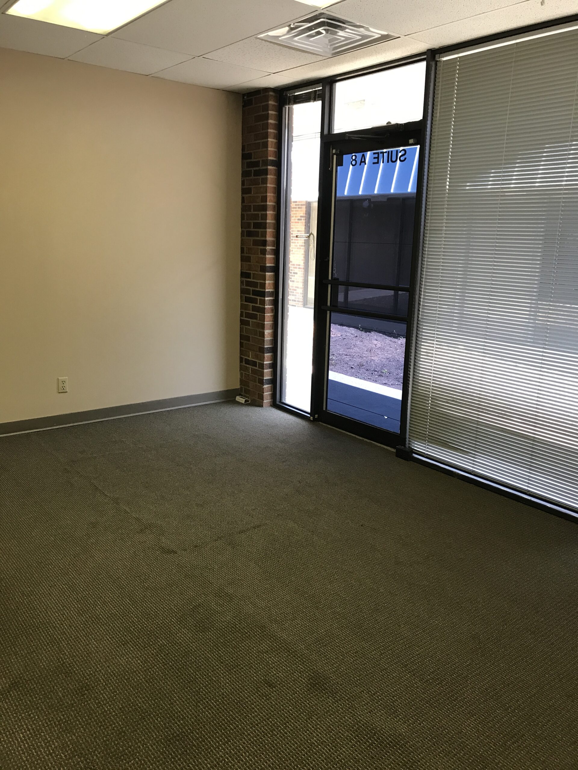 Empty room with green carpet and large windows letting in natural light.