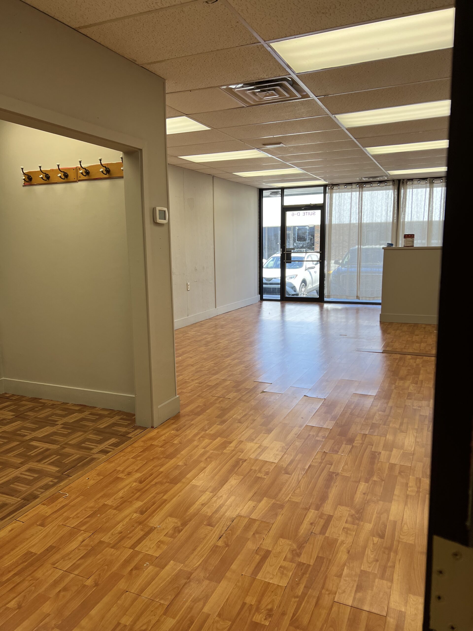 Empty office space with wooden flooring and large windows.